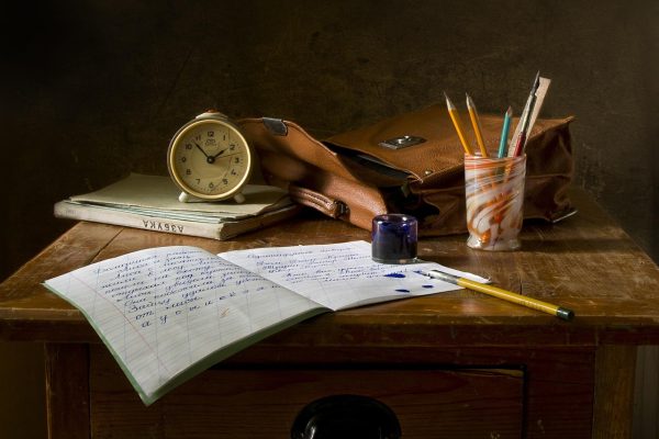 家长在餐桌边用手指滑动手机屏幕查看学校通作业反馈，孩子在旁边写作业